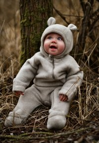 Beiger Kapuzen-Einteiler aus weichem Stoff, mit Bärenohren an der Kapuze, Reißverschluss vorne und gemütlichen Stiefeln. Vor natürlichem Hintergrund.