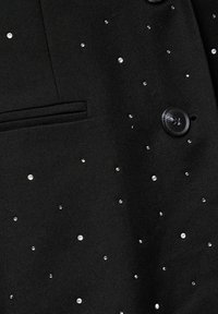 Juodas švarkas, pasižymintis klasikiniu dizainu, su išmėtytais deimanto akmenimis ir priekinę kišenę. Juoda saga.