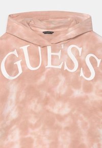Helle rosa TIE-DYE-Hoodie mit "GUESS" in großen weißen Buchstaben quer über die Brust gedruckt und einer Kapuze oben.