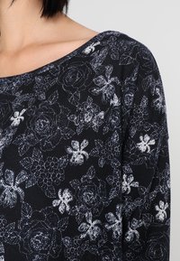 Maglione nero con motivo floreale bianco, con scollo ampio e tessuto strutturato. Caratterizzato da una vestibilità morbida.