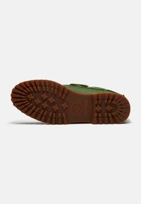 Botte verte allongée sur le côté, montrant une semelle en caoutchouc marron avec des crampons profonds et des logos de la marque embossés sur la semelle.
