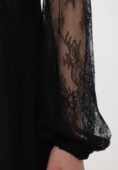 Rochie neagră cu mâneci din dantelă transparentă, cu modele florale și manșete elastice, accentuată de un corset texturat.