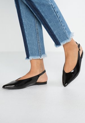 Black patent leather slingback flats with pointed toe, low heel, and cutout sides. Worn with frayed hem blue denim jeans.