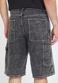 Shorts cargo en denim noir avec une texture délavée, dotés de deux poches arrière et d'une poche latérale, de coutures renforcées et de surpiqûres blanches contrastantes.