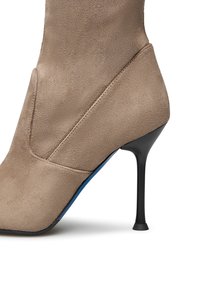 Stivale alla caviglia in suede beige con punta affilata, tacco a stiletto nero e accento blu lungo la suola. Texture liscia e design minimalista.