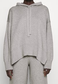 Szara bluza z kapturem z miękkiego materiału, o luźnym kroju, długich rękawach, przedniej kieszeni i regulowanym kapturem na sznurku.