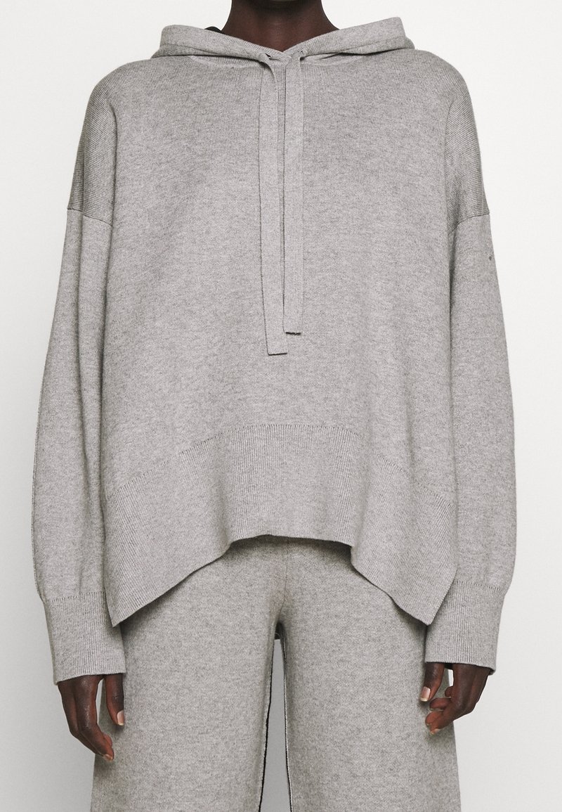 Szara bluza z kapturem z miękkiego materiału, o luźnym kroju, długich rękawach, przedniej kieszeni i regulowanym kapturem na sznurku.