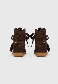 Par de ténis de cunha em camurça castanho escuro com detalhes em tachas douradas na parte traseira e solas em borracha cor de goma, vistos de trás.