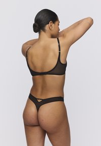 Conjunto de sujetador y tanga de malla negra. El sujetador cuenta con tirantes delgados ajustables, un corte sutil en la parte posterior y un cierre de gancho.