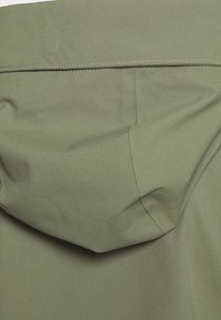 Tissu vert olive avec une finition lisse et mate et des coutures visibles, affichant une capuche et un design sans couture.