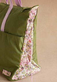 Geantă din nailon verde, cu o parte decorată cu un model floral, accente roz și detalii din dantelă. Include un sistem de închidere cu fermoar și două mânere.