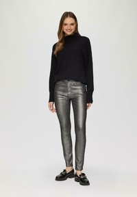 Czarny sweter z golfem, metaliczne srebrne dopasowane dżinsy i czarne loafersy z masywną podeszwą. Model stoi na jasnym tle.