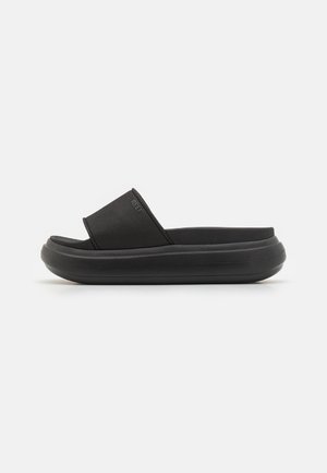 Sort slidesandal med tyk polstret sål og bred rem over toppen, placeret sidelæns på en hvid baggrund.