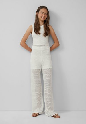 Witte gebreide twee-delige outfit met een mouwloos topje en wijde broek, die een opengewerkt ruitpatroon en gestructureerde stof laat zien.