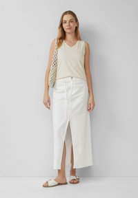 Weißer Denim-Maxi-Rock mit einem zentralen Schlitz, kombiniert mit einem hellbeigen ärmellosen Oberteil. Accessoires bestehen aus einer Häkel-Tasche und flachen Sandalen.