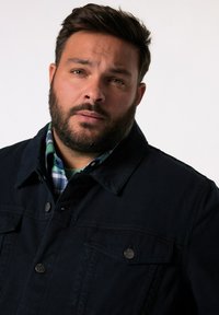 Námořnická modrá džínová bunda s dvěma předními kapsami a stříbrnými knoflíky, navrstvená přes košili s kulatým výstřihem v zeleno-modrém kostkovaném vzoru.