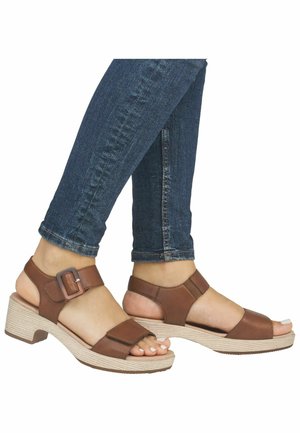 Brown leather sandals with an open toe design, adjustable buckle, and a textured, light-colored platform heel. Worn with dark jeans.