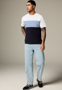 Herr T-shirt: vit topp med horisontella ljusblå och mörkblå ränder, bomullsblandning. Kombinerad med ljusblå jeans och svarta skor.