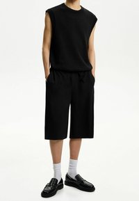 Svart ärmlös tröja i strukturerad tyg; svarta shorts med sidofickor; matchat med svarta loafers och vita strumpor.