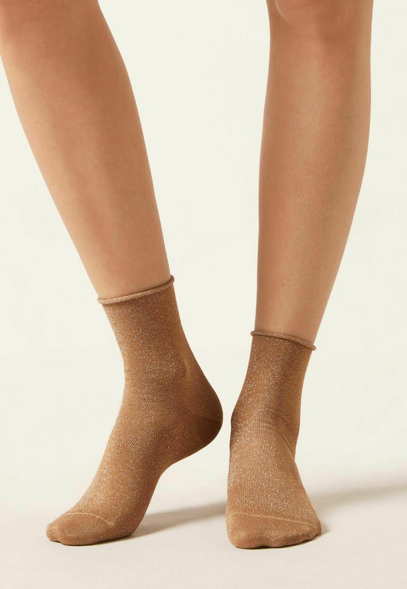 Calcetines de tobillo marrones con un acabado brillante, que presentan un puño acanalado y una textura suave. Hilos brillantes crean un efecto deslumbrante.