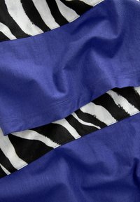 Tejido de algodón con atrevidas rayas de cebra en blanco y negro, combinado con una sección azul suave, creando una apariencia texturizada en capas.