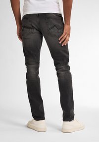 Mustat slim-fit farkut, joissa on kulunut pinta, kaksi takataskua, joissa on siksak-ompelua, kulunut ilme, yhdistettynä vaaleanvärisiin tennareihin.