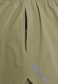 Hellolivgrüner Stoff mit einer vertikalen schwarzen Reißverschlusstasche und blauem Text "HALO 198819721981" in der Nähe des Bodens gedruckt.