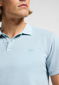 Ljusblå polo skjorta i texturerat tyg med krage och två knappar. Har en liten broderad "Lee"-logotyp på bröstet.
