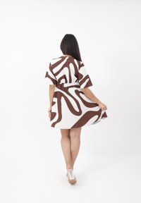 Braun-weißer gemusterter Kleid mit kurzen Ärmeln, tailliertem Schnitt und einem fließenden Rock, der aus einem glatten Stoff mit leichter Textur besteht.
