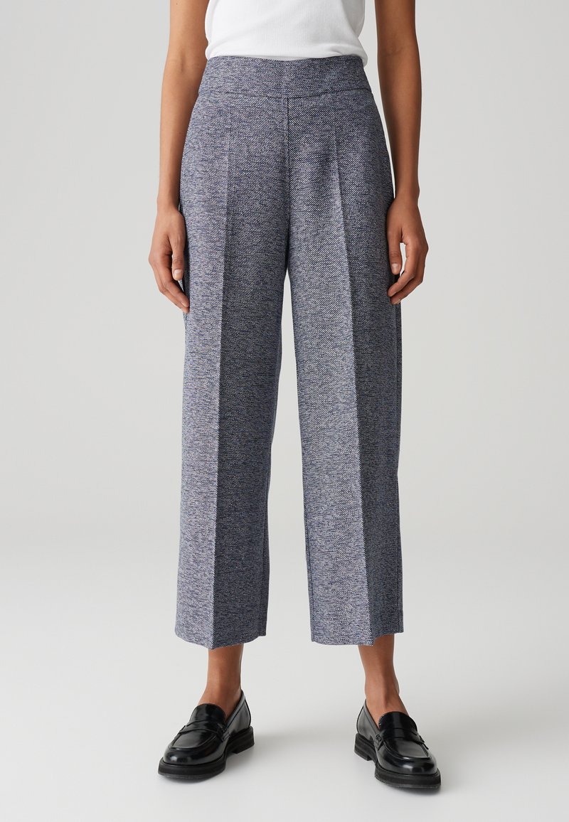 Pantalons à jambes larges dans un motif chevron texturé bleu et gris avec une taille haute et des plis. Associés à des mocassins noirs.