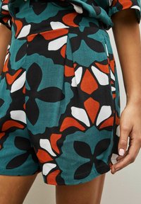 Shorts à motif floral avec un fond en teal, accents noirs, orange et blancs ; plis et coupe décontractée ; texture de tissu douce.