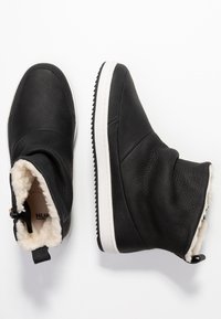 Botas de tobillo negras hechas de cuero texturizado con un suave forro de piel blanca, que cuentan con una suela de goma blanca y un lazo de tela en el talón.