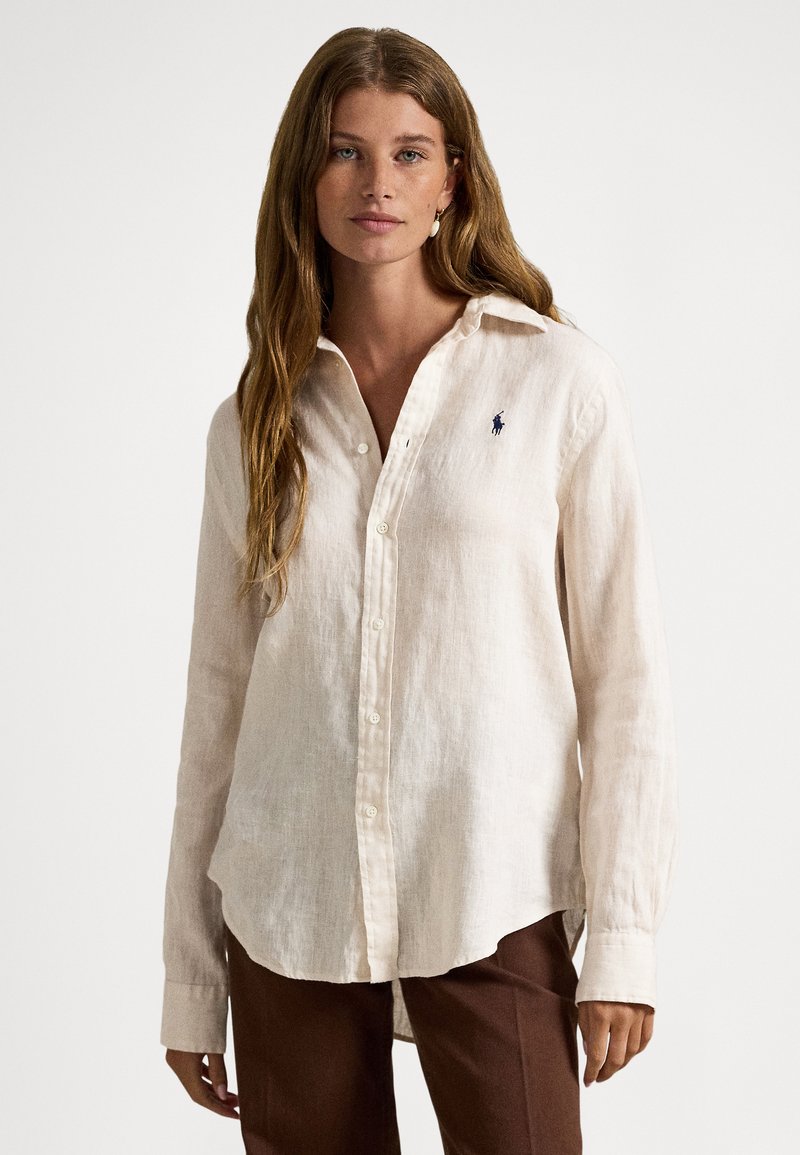 Light beige linen long-sleeve shirt with button-down collar, featuring a small blue logo on the chest and a curved hem.