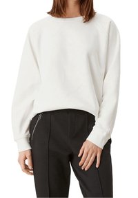 Felpa bianca con una texture morbida, colletto a costine e spalle scese, abbinata a pantaloni neri con texture e dettagli con tasche con zip.