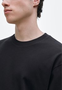 Svart bomulls-t-shirt med rund halsringning och korta ärmar, som visar en slät textur med minimala sömnadsdetaljer.