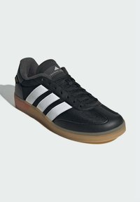 Black athletic shoe featuring mesh and synthetic leather, with three white stripes, textured surface, and a gum rubber sole.