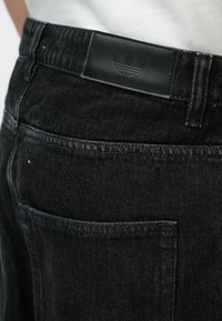 Μαύρα τζιν από τζιν με λεία υφή, που διαθέτουν δερμάτινο ταμπελάκι στη μέση με λογότυπο, λεπτομέρειες στην πίσω τσέπη και μινιμαλιστική ραφή.