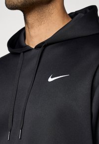 Μαύρο φούτερ Nike με λεία υφή. Διαθέτει λευκό κεντητό λογότυπο στη αριστερή πλευρά του στήθους και λεπτομέρειες με κορδόνια στην κουκούλα.