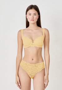 Reggiseno in pizzo giallo con bordi scallop e motivi floreali, abbinato a mutandine in pizzo coordinate. Entrambi presentano una finitura delicata e testurizzata.