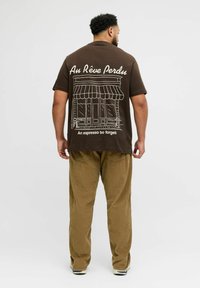 Brown cotton t-shirt featuring white line art of a café on the back, complemented by text. Paired with loose olive green corduroy pants.