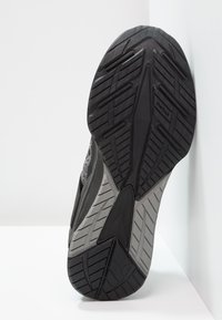 Semelle de chaussure de sport noire avec motifs texturés, comprenant des rainures d'adhérence et une section lisse grise ; marquée du logo « Evertrack ».