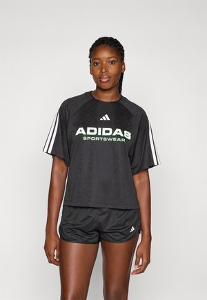 Camiseta deportiva negra de manga corta con un patrón texturizado, que presenta un logo verde y tres rayas blancas en cada manga. Combinada con pantalones cortos negros.