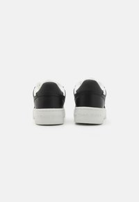 Sneakers low-top in pelle nera con suola in gomma bianca e branding sul tallone. Presentano un classico design con lacci e accenti a contrasto.