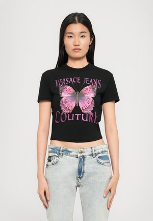 Black cropped t-shirt with short sleeves featuring a pink butterfly graphic and "VERSACE JEANS COUTURE" text in bold pink font.