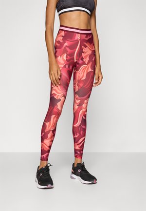 Leggings u crveno-ružičastom apstraktnom cvjetnom uzorku, visoki struk, izrađene od rastezljivog materijala. Uparene s crnim sportskim cipelama.