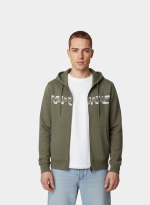 Oliwkowa bluza z kapturem na zamek błyskawiczny, z dwiema przednimi kieszeniami, kapturem ze sznurkiem i dużym szarym napisem "KAPORAL" na piersi. Materiał mieszanka bawełny.