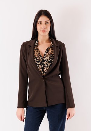 Blazer marrone sartoriale con collo sciallato, chiusura con un solo bottone e maniche lunghe, indossato sopra una camicia a stampa leopardata e jeans scuri.