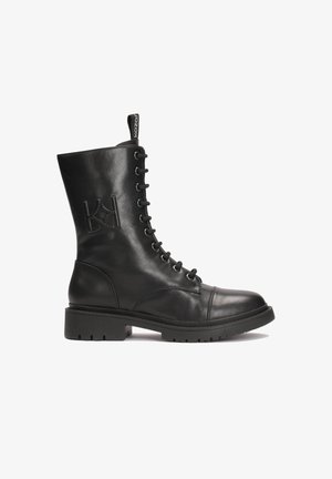 Bottine en cuir noir à lacets, avec un bout arrondi et une semelle en caoutchouc épaisse. Présente un logo embossé sur le côté et une languette.