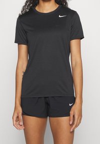 Camiseta deportiva negra hecha de tejido transpirable, con mangas cortas, cuello redondo y un pequeño logo blanco de Nike en el pecho.
