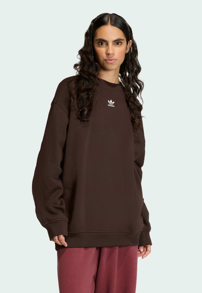 Brown sweatshirts with a loose fit, long sleeves, and a small white logo on the chest, paired with red sweatpants. Soft texture.